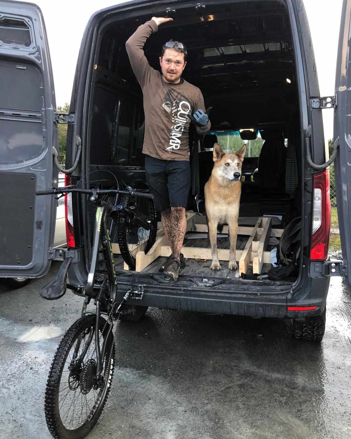 Kyle, GRBX founder, standing in the back of his van with his dog, a muddy mountain bike leaning against the tailgate